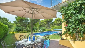 En terrasse med pool, havemøbler og stor parasol.