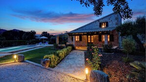 Una casa de piedra con piscina, rodeada por un jardín cuidado y un cielo despejado.