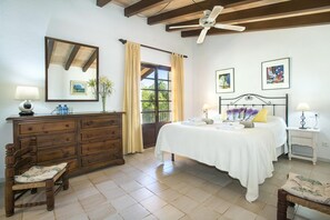 Quarto com cama, cômoda, cadeira, ventilador de teto e obras de arte nas paredes.