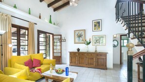 A bright living room with a yellow sofa, wooden cabinet, and a staircase. - Ca'n Puput - Two Bedroom Villa, Sleeps 4 (Mallorca)