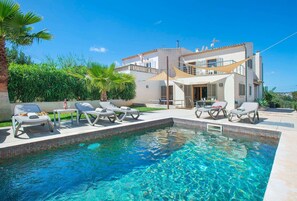 Uma área de piscina moderna com espreguiçadeiras e uma piscina azul cristalina, cercada por um edifício branco com varanda.