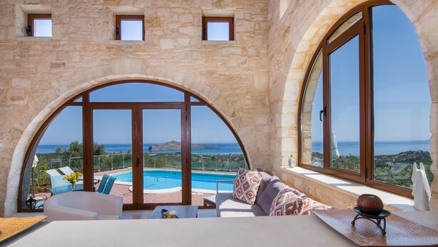 A luxurious room with a stone wall, large arched windows, a pool, and a view of the sea. - Villa Kourouni - Three Bedroom Villa, Sleeps 6 (Crete)