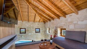 A rustic stone-walled room with a wooden ceiling, a round wooden table with wine glasses and a bottle, a sofa, and a view of a pool through a glass door. - Villa Kourouni - Three Bedroom Villa, Sleeps 6 (Crete)
