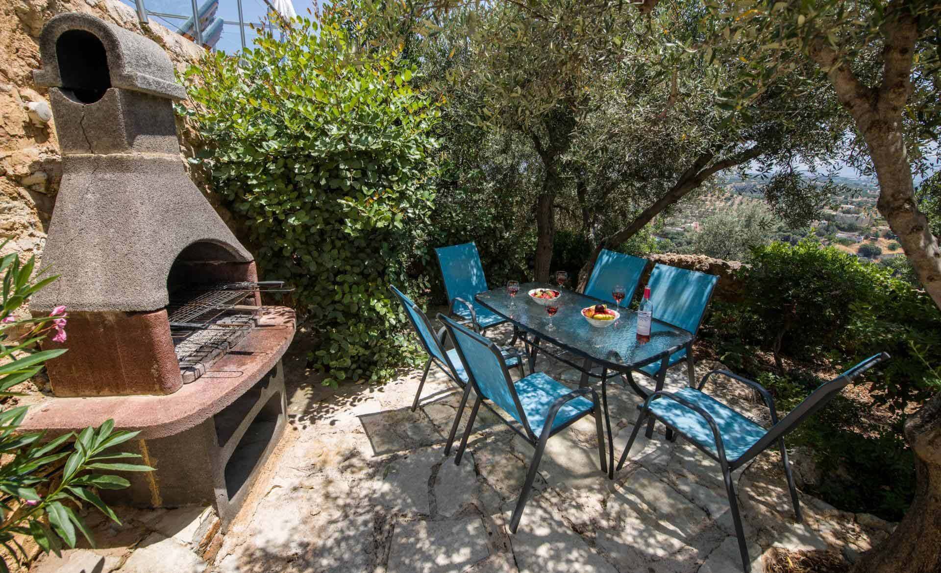 An outdoor patio with a stone-built grill, a table with chairs, and a view of a hilly landscape.