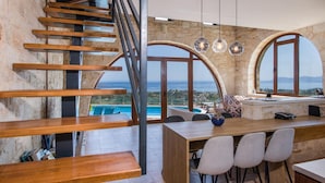 A modern kitchen with a view of the sea, a dining area with a pool view, and a wooden staircase. - Villa Kourouni - Three Bedroom Villa, Sleeps 6 (Crete)