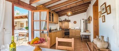A rustic kitchen with wooden beams, a dining area with a table set for two, and a view of the outside patio.