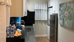 A compact kitchen with white cabinets, a stainless steel refrigerator, and a black tiled backsplash.