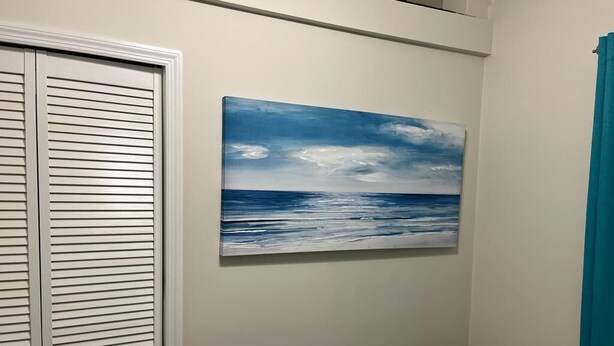 A room with a white closet, a painting of a seascape, and a teal curtain.