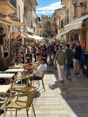Eine belebte Straße mit Außenbereich, einem Marktstand und einem historischen Bogen im Hintergrund.