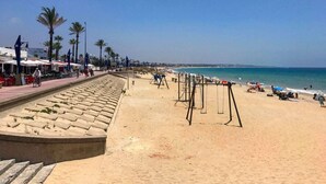 Una playa con un paseo arenoso, palmeras y sombrillas.