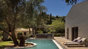Une piscine dotée d’une pergola et d’un espace détente, entourée d’arbres et d’un bâtiment.