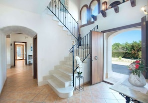 A spacious interior with a grand staircase, a wooden door leading outside, and a view of the outdoors.