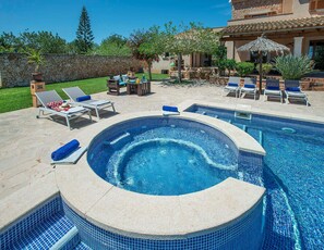 Une piscine avec un jacuzzi, des chaises longues et un mur en pierre.