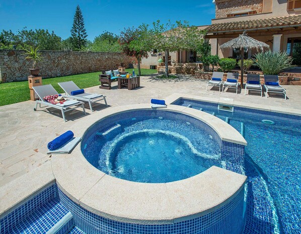 A swimming pool with a hot tub, lounge chairs, and a stone wall.