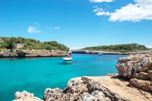 A rocky coastline with clear turquoise waters and a boat anchored in the middle.