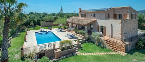 A two-story house with a swimming pool, outdoor seating, and a stone facade.