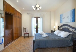 Une chambre à coucher comprenant un lit, une chaise, une armoire, un luminaire au plafond, une table de chevet et un tableau accroché au mur.