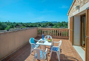 Un balcon avec une table et des chaises, une bouteille et un saladier rempli de fruits.