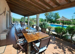 An outdoor dining area with a long wooden table and chairs, a pool, and a covered patio.