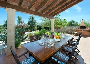 Un espace de restauration en plein air avec une longue table en bois dressée pour un repas, entourée de chaises dotées de coussins à motifs.