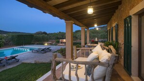 A covered outdoor seating area with a pool, lounge chairs, and a wooden bench with cushions.