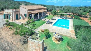 A Mediterranean-style villa with a swimming pool, outdoor seating, and a view of the surrounding hills.