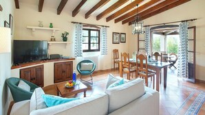 A spacious living area with a sofa, television, wooden dining table, and chairs. - Ca'n Pep - Two Bedroom Villa, Sleeps 4 (Mallorca)
