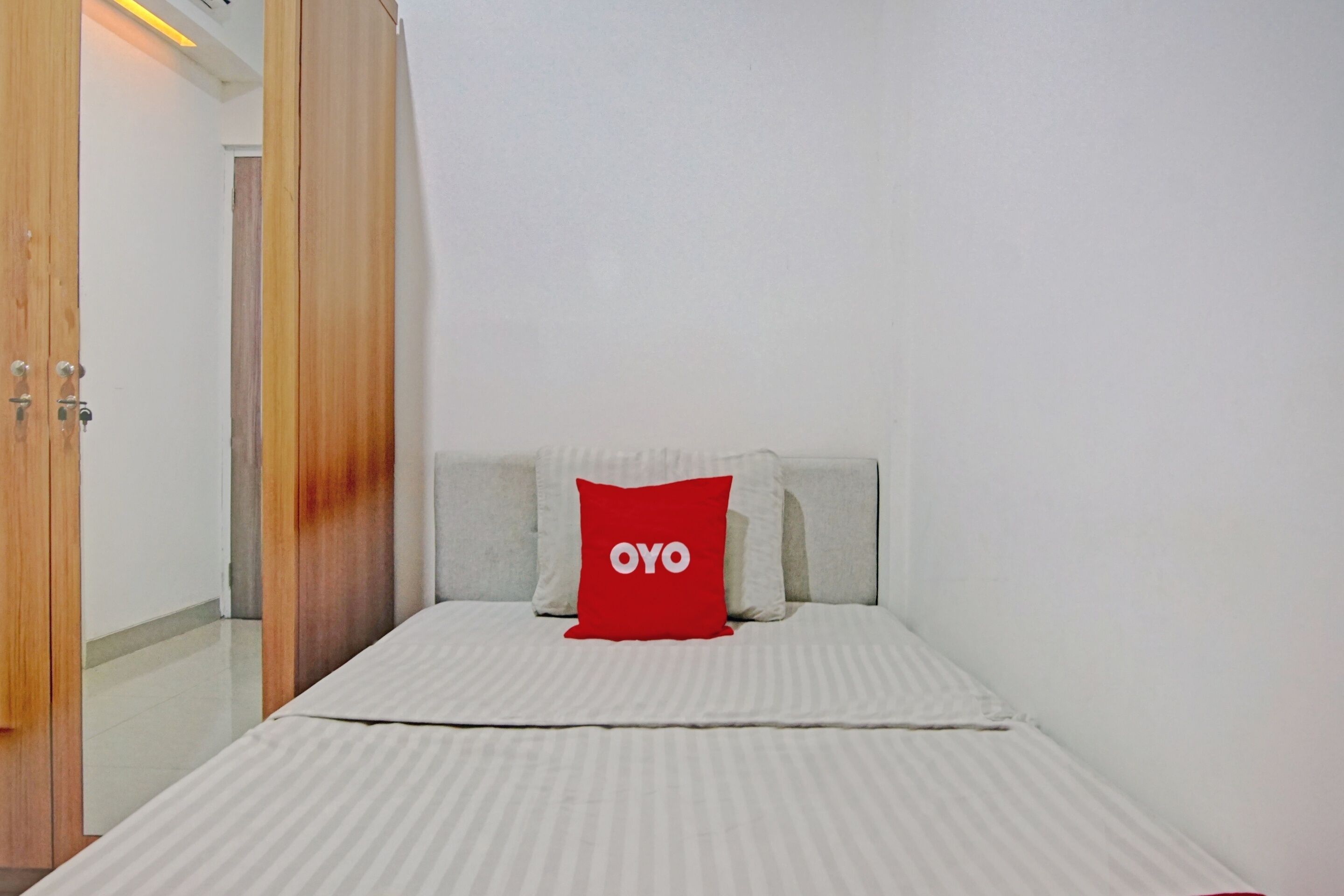Un dormitorio con cama, almohada roja con la palabra "OYO" y un armario de madera.
