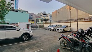 A parking area with multiple cars and motorcycles, a building with a satellite dish, and a tree in the foreground. - Capital O 90432 Family Residence Near SCBD, Ciwalk, Mall Casablanca (Jakarta)