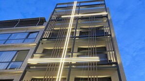 A multi-story building with a modern architectural design, featuring balconies with railings and illuminated by vertical light strips. - Nema Hotel Athens (Athens)