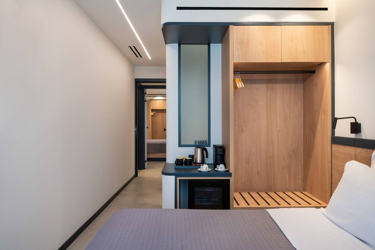 Una habitación de hotel moderna con una cama, un escritorio pequeño con cafetera, un espejo y un armario.
