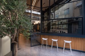 A modern bar area with a large window, wooden paneling, and three white bar stools. - Nema Hotel Athens (Athens)