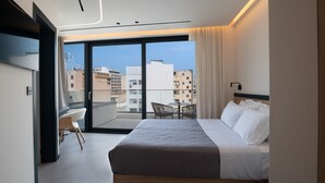 A modern hotel room with a large bed, a desk, and a chair, a balcony with a view of the city, and a TV mounted on the wall. - Nema Hotel Athens (Athens)