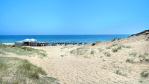 A beach with a row of beach chairs and umbrellas, a small structure with a sign, and a clear blue sky.