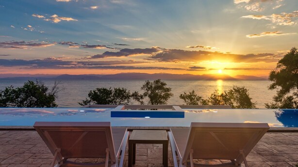 A sunset view from an infinity pool with two lounge chairs facing the sea.
