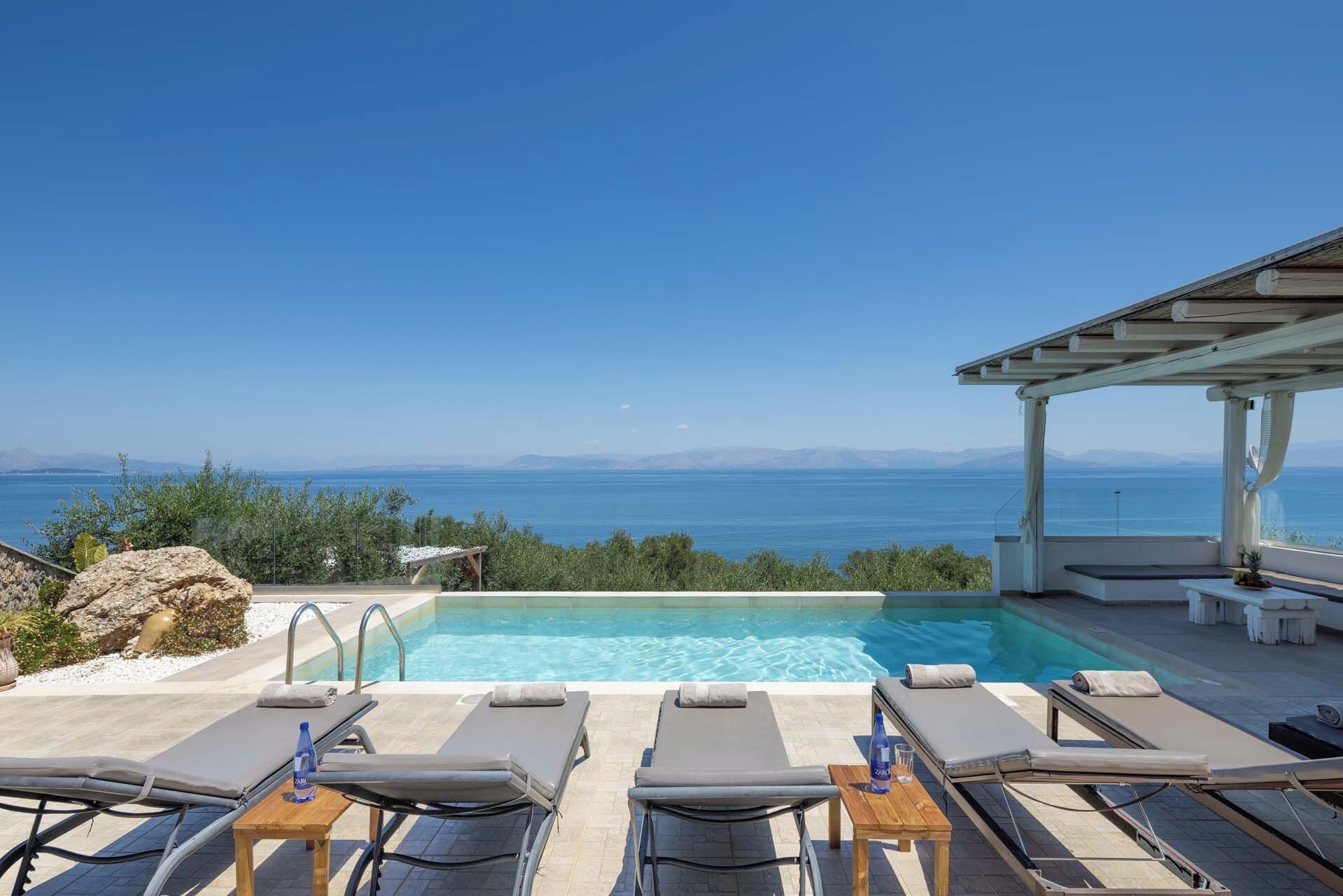 A pool area with lounge chairs and a view of the sea.