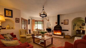 A cozy living room with a fireplace, red sofas, and a chandelier. - El Molino del Pilón - Five Bedroom Villa, Sleeps 10 (Arcos de la Frontera)