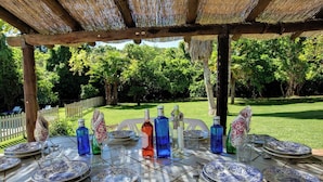 An outdoor dining area with a thatched roof, surrounded by lush greenery. - El Molino del Pilón - Five Bedroom Villa, Sleeps 10 (Arcos de la Frontera)