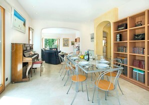 A spacious dining area with a piano, a long table set for six, and a bookshelf filled with books and records.