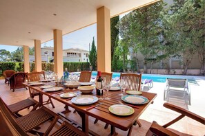 A dining area with a table set for six, overlooking a swimming pool and a garden.