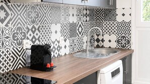 A modern kitchen with grey cabinets, a black coffee machine, a white dishwasher, and patterned tiles.