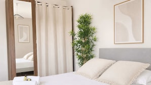 A hotel room with a bed, white towels, a mirror, a plant, and a framed abstract artwork.