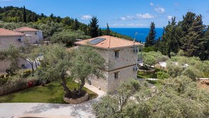 Un bâtiment en pierre, doté d’un toit en tuiles, entouré d’arbres et offrant une vue sur la mer.