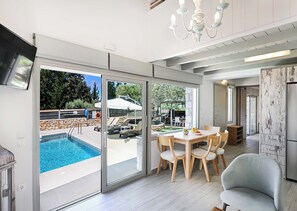 Una cucina moderna con forno integrato, una zona pranzo con tavolo e sedie, e un'ampia porta scorrevole in vetro che dà su un'area piscina esterna.