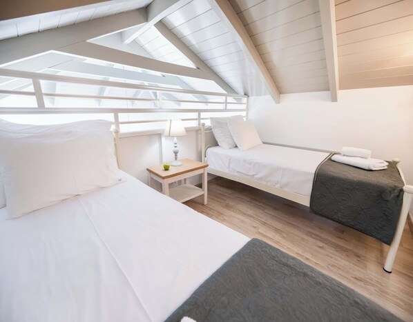 A room with two beds, a small table with a lamp, and a window with a view.