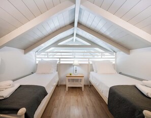 Un dormitorio de ático pequeño y acogedor con dos camas individuales, una mesita de noche con lámpara y un tragaluz.
