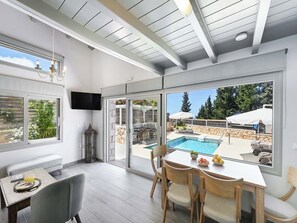 Una camera moderna con vista sulla piscina, un'area pranzo con sedie e un televisore montato a parete.