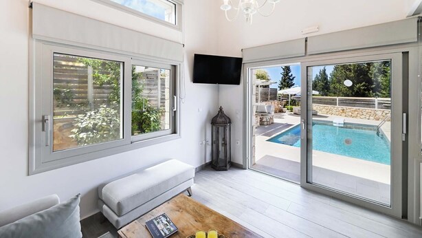 Un salon moderne avec un canapé, une table basse sur laquelle repose un livre, un téléviseur et une vue sur la piscine.