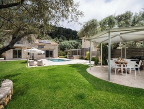 A backyard with a swimming pool, a covered patio area, and a stone house.