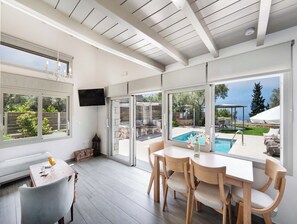 A modern interior with a pool view, a dining area, and a television. - Mirto - Three Bedroom Villa, Sleeps 6 (Tsoukalades)